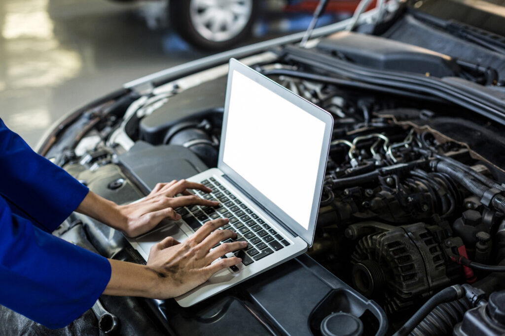 Mechanic using laptop over engine