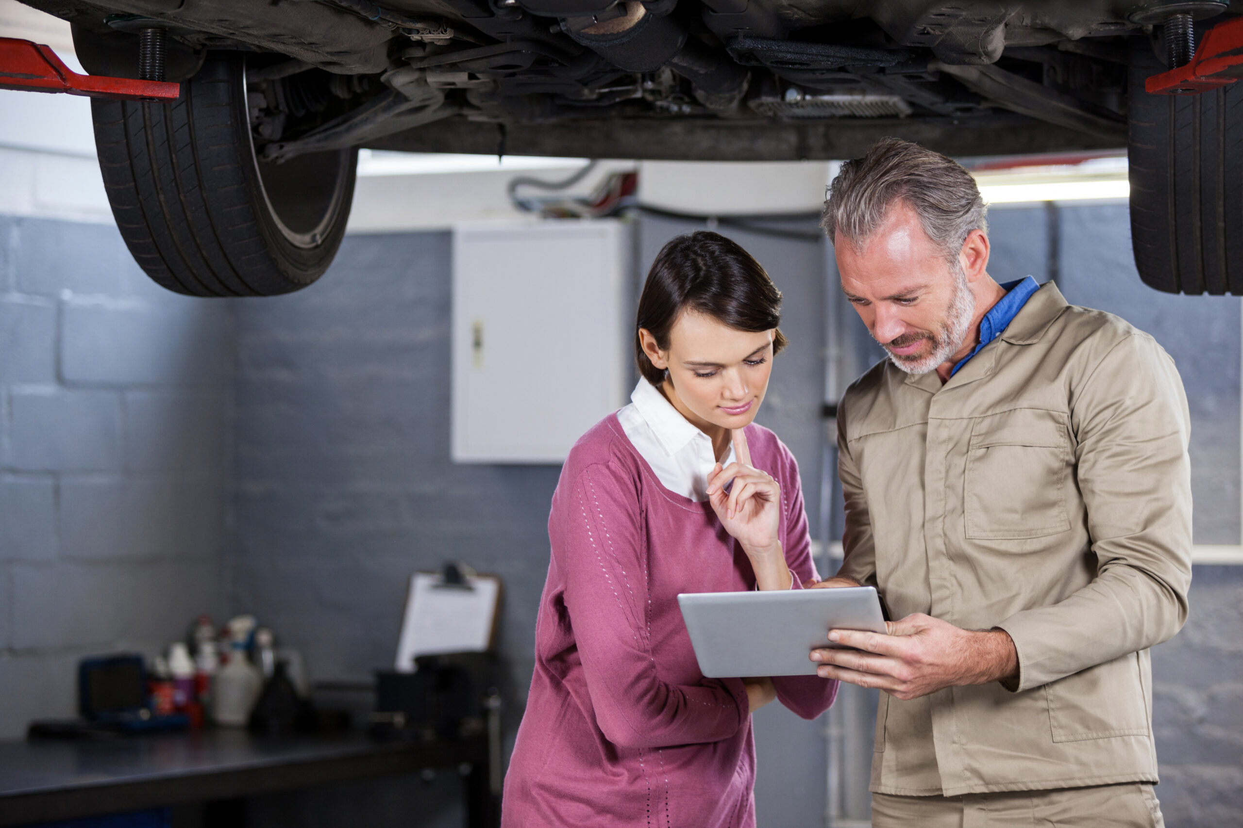 Mechanic reviewing tablet with customer, car lift