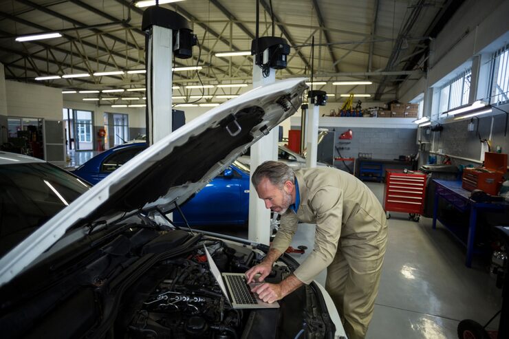 Mechanic diagnosing car engine with laptop